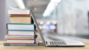 Stack of books with laptop on wooden table